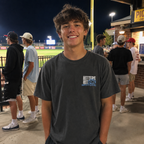 Teen wearing a pepper Beast adult baseball T-shirt at a nighttime baseball game.