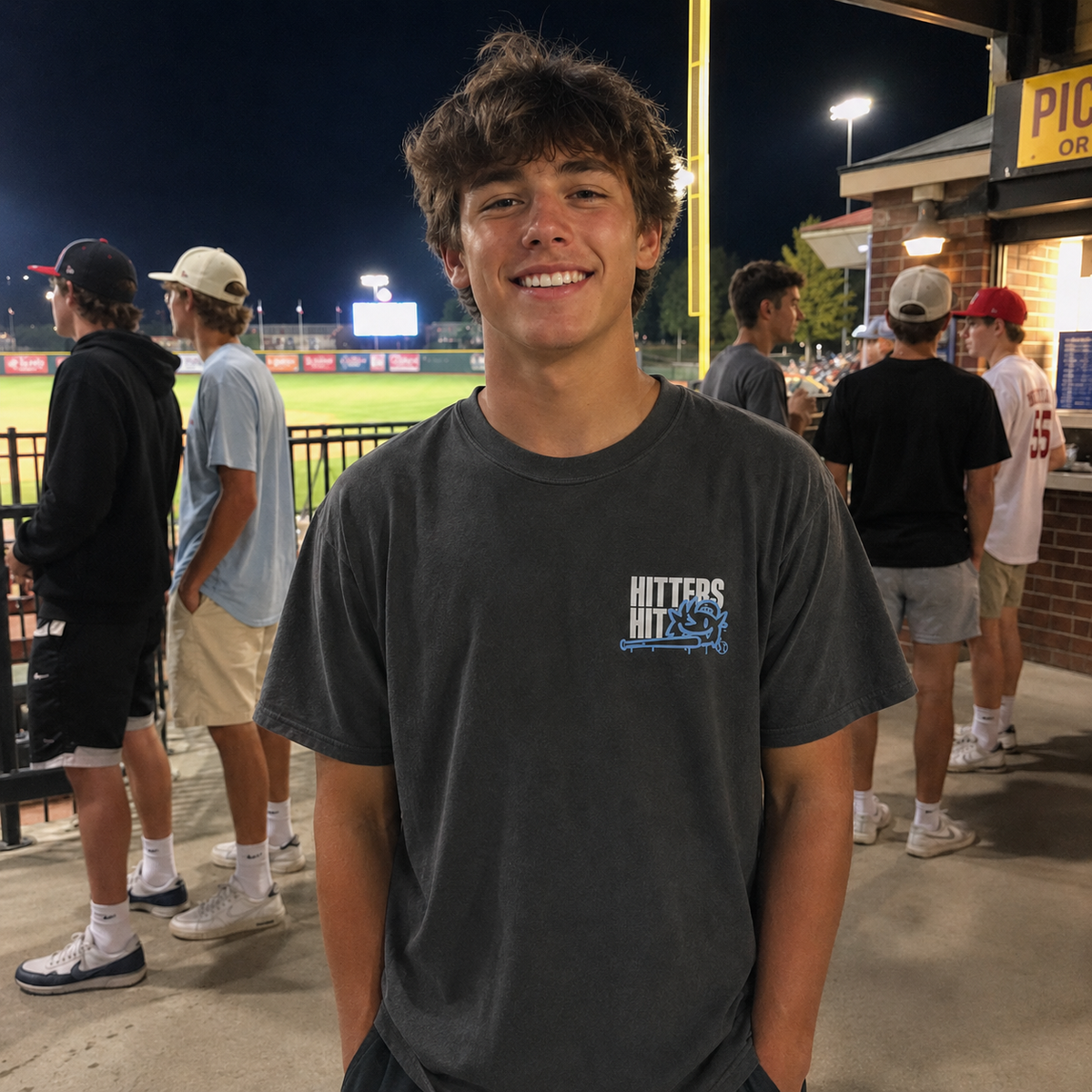 Teen wearing a pepper Beast adult baseball T-shirt at a nighttime baseball game.