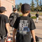 Boy wearing black youth baseball T-shirt with large Beast baseball back graphic near the field.