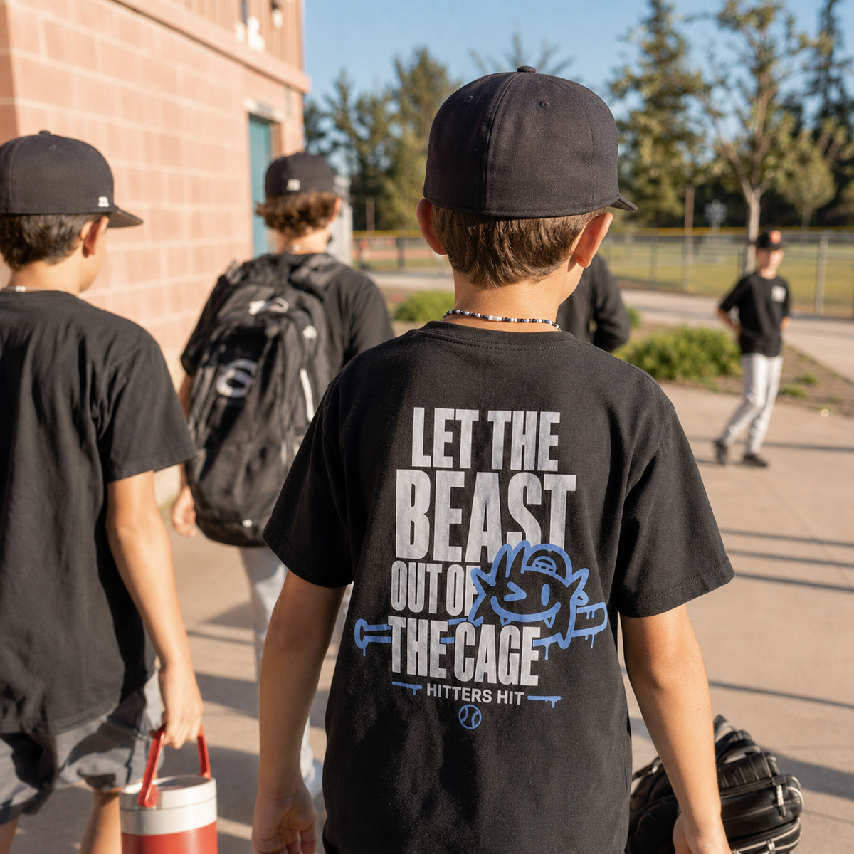 Boy wearing black youth baseball T-shirt with large Beast baseball back graphic near the field.