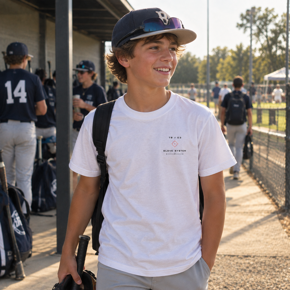 Youth baseball player wearing a white Built for the Game Glove T-shirt with the small TB 03 Glove System left-chest graphic at a baseball field.