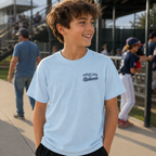 Boy wearing the chambray Late Nights at the Ballpark youth baseball T-shirt with small left chest design at a baseball field.