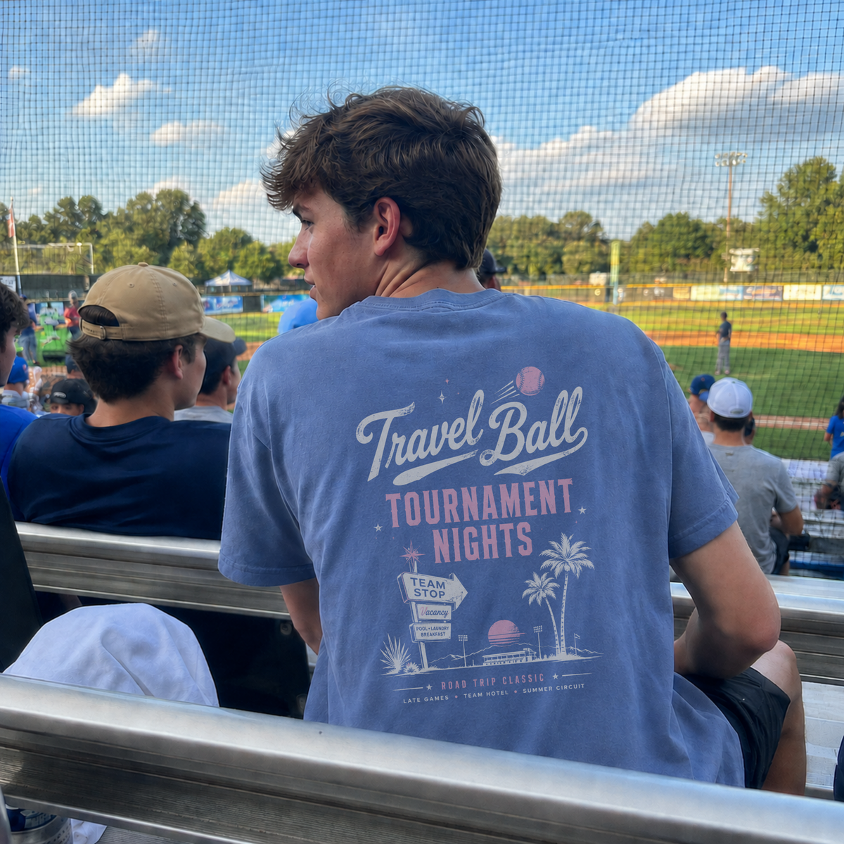 Teen boy wearing the Washed Denim adult travel ball T-shirt at a baseball field, showing the large Tournament Nights graphic on the back.