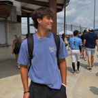 Teen boy wearing the Washed Denim adult baseball T-shirt at a baseball complex, showing the small Travel Ball left-chest graphic.