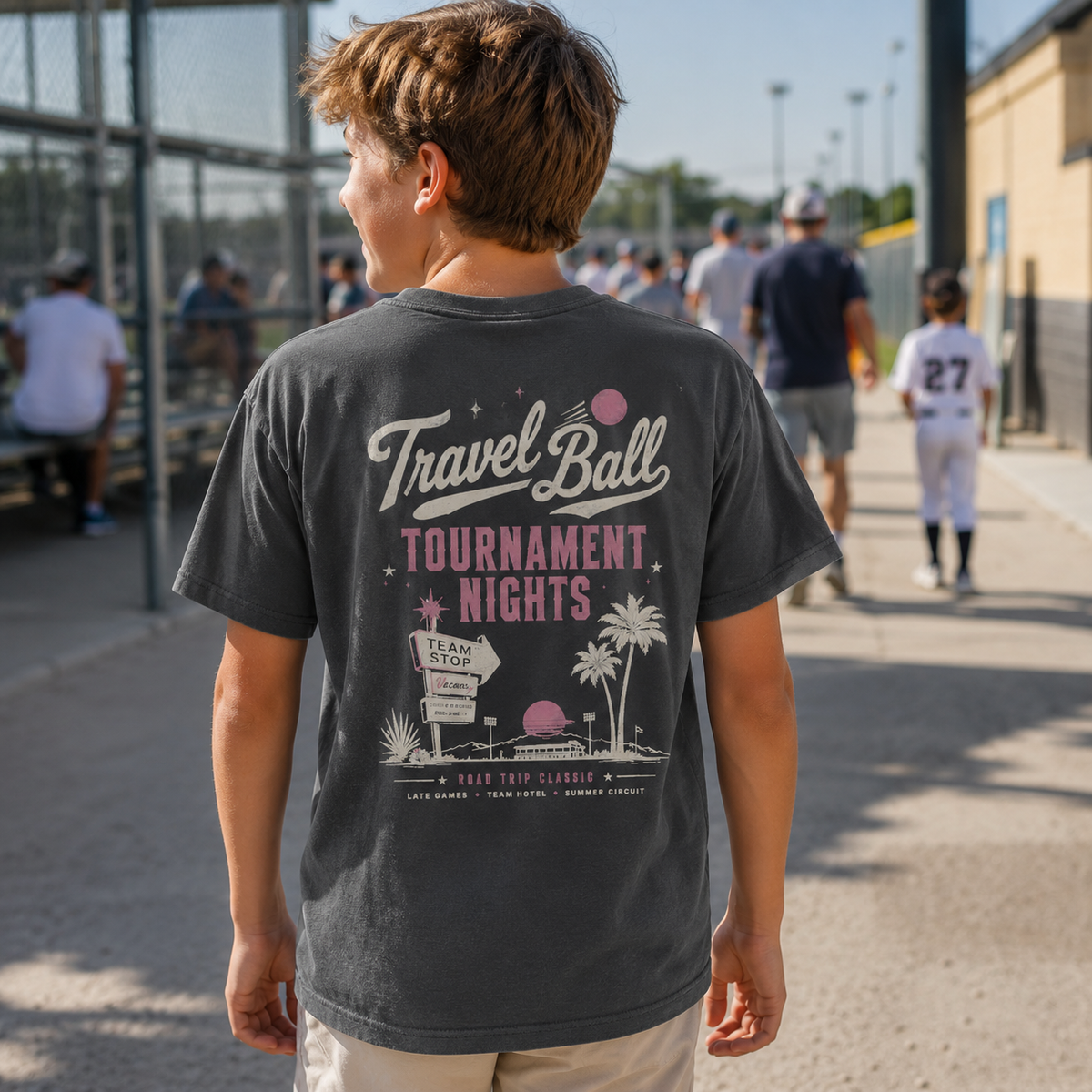 Youth boy wearing the Pepper baseball T-shirt at a ballpark, showing the large vintage Travel Ball Tournament Nights graphic on the back.