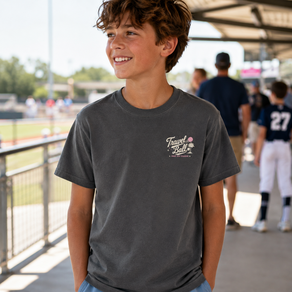Youth boy wearing the Pepper travel ball T-shirt at a baseball complex, showing the small Travel Ball chest graphic.