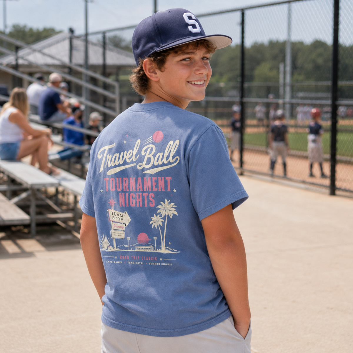 Youth boy wearing the Washed Denim travel ball shirt at a baseball complex, showing the large vintage Tournament Nights back graphic.