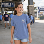 Youth girl wearing the Washed Denim baseball T-shirt at a ballpark, showing the small Travel Ball left-chest graphic.